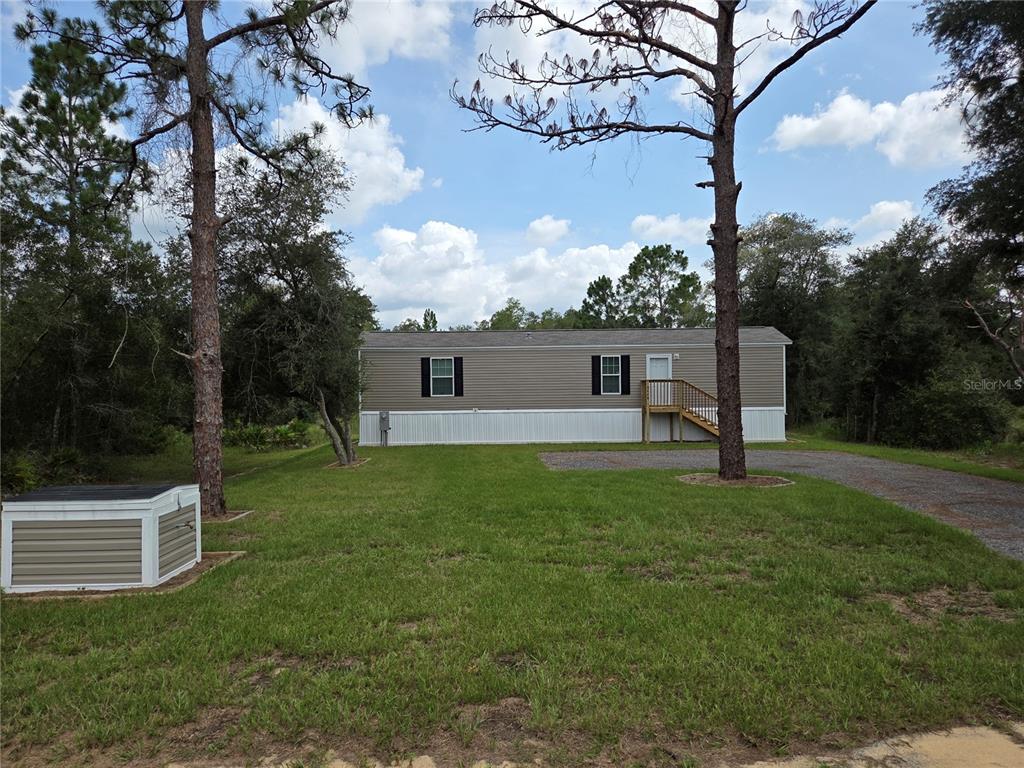 A single-story manufactured home with tan siding sits on a grassy lot with trees — 9448 ROUSSEAU STREET, WEBSTER, FL