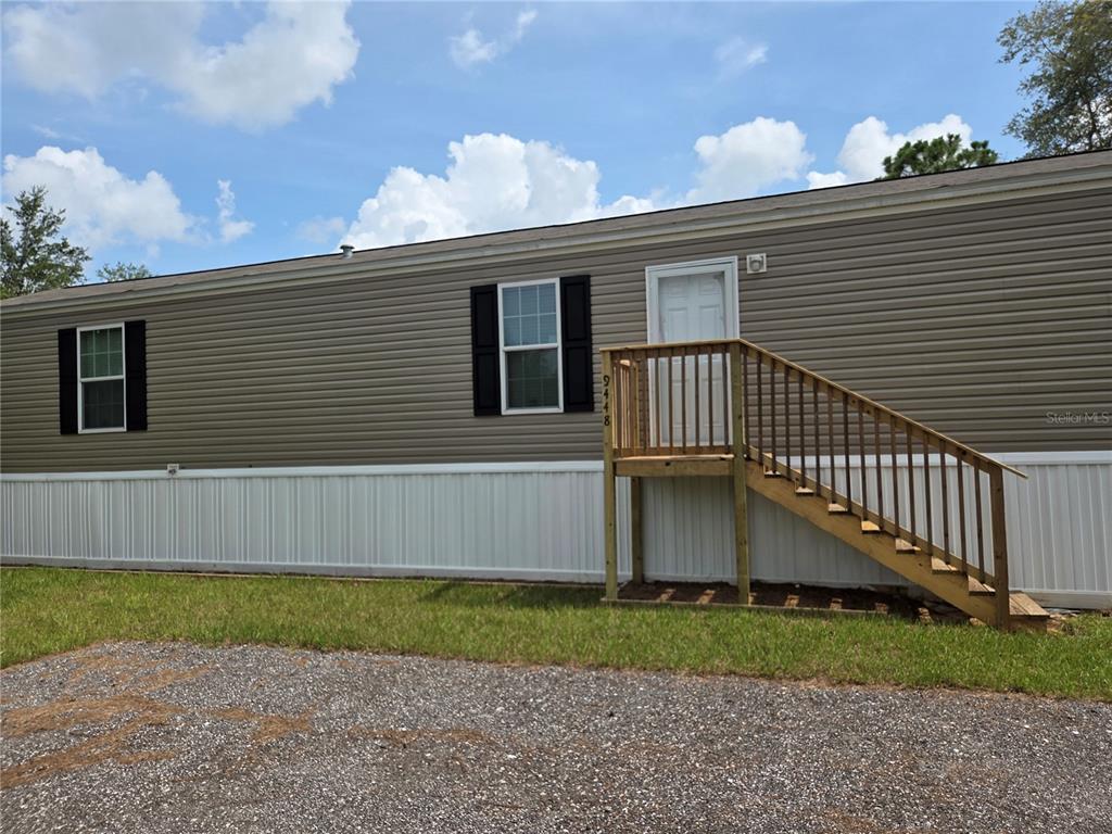 A tan mobile home with white skirting and a wooden staircase leading to the front door — 9448 ROUSSEAU STREET, WEBSTER, FL
