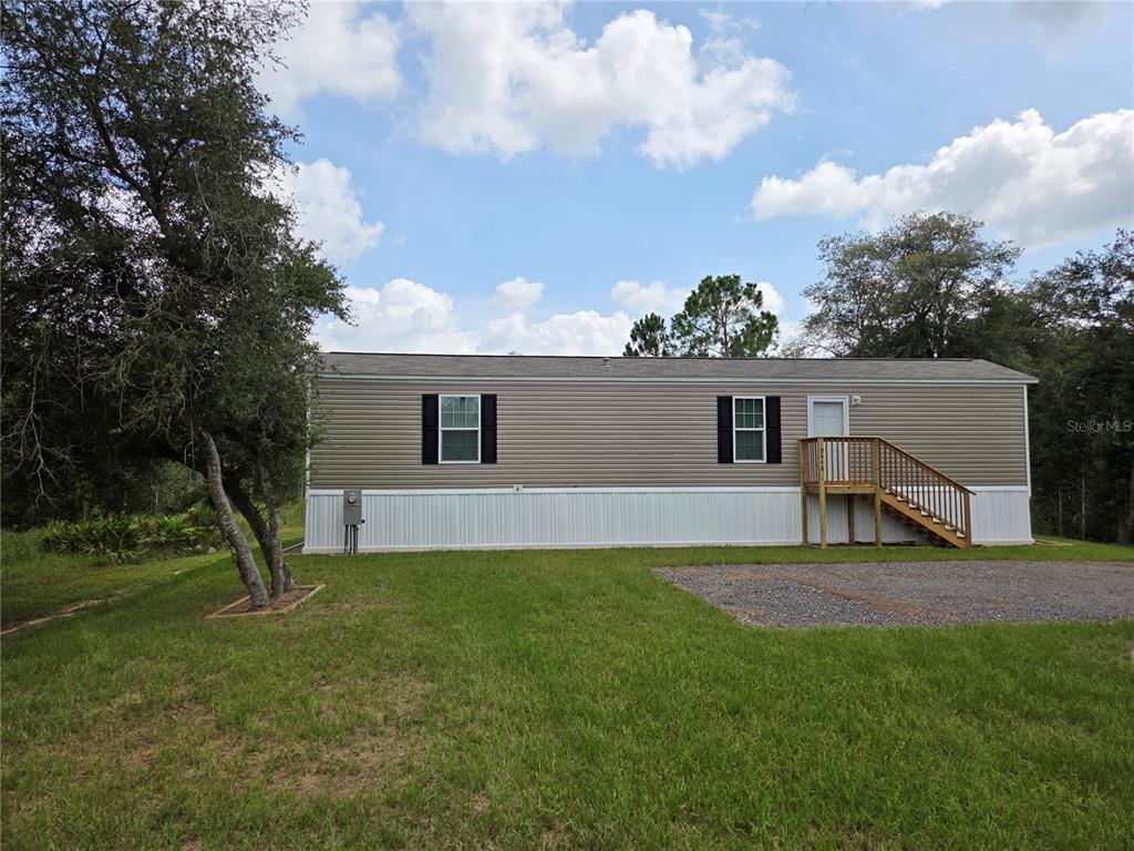 A single-story manufactured home with tan siding, white skirting, and a wooden staircase — 9448 ROUSSEAU STREET, WEBSTER, FL