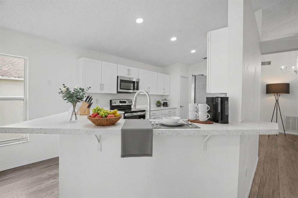 A kitchen features white cabinets, a speckled countertop island, and stainless steel appliances — 419 SAINT ANNS DRIVE, WINTER HAVEN, FL