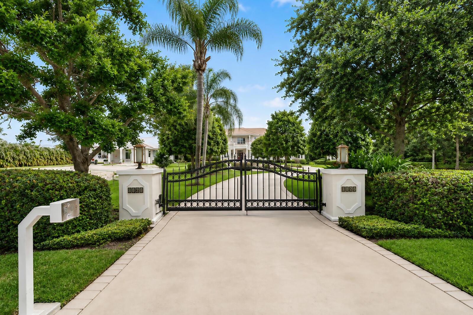 A paved driveway leads to a gated entrance with white pillars and lush landscaping — VERO BEACH, FL