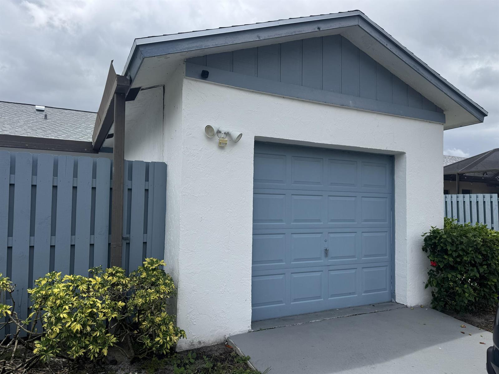 A white garage with a blue door and matching trim under a cloudy sky — 1204 Timberlane Circle # 12d, FL 33463, FL