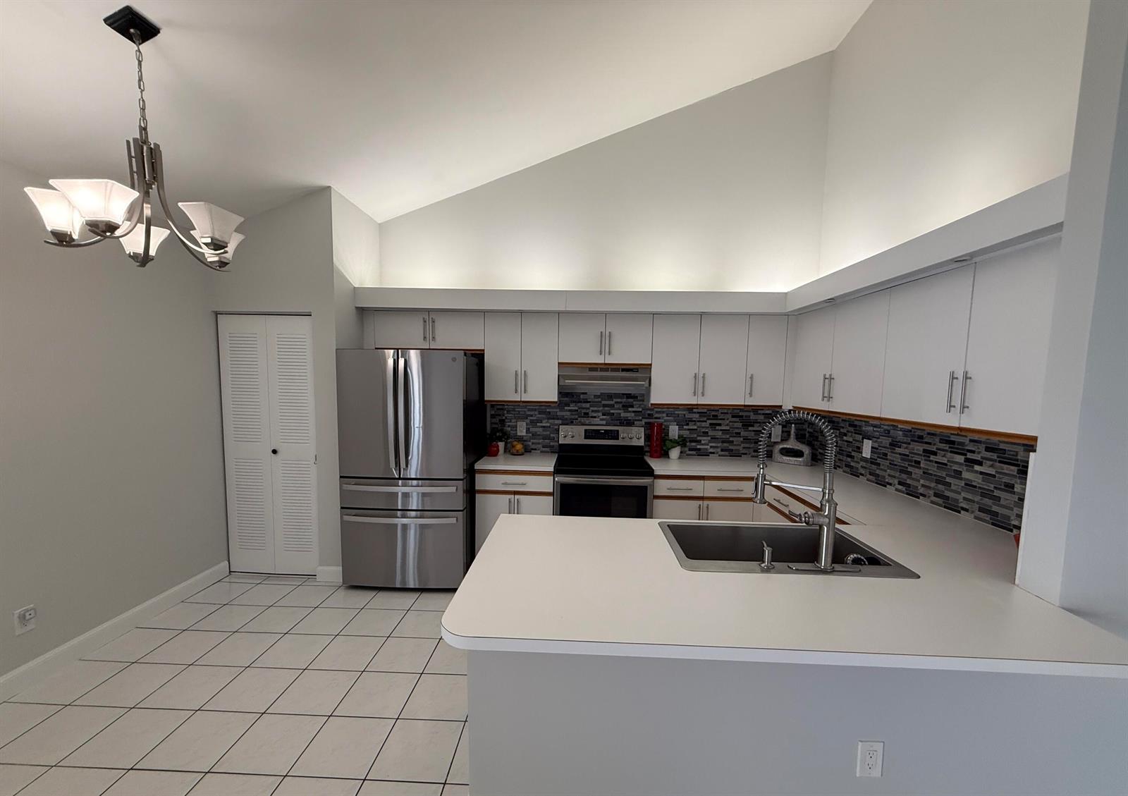 A kitchen features white cabinets, stainless steel appliances, a tiled backsplash, and a vaulted ceiling — 1204 Timberlane Circle # 12d, FL 33463, FL