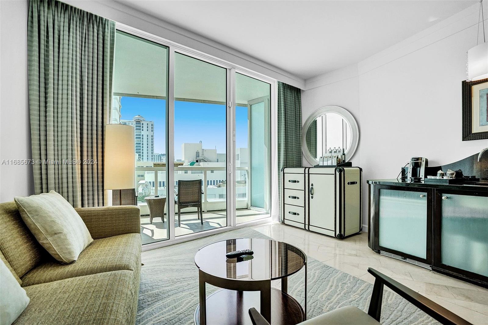 A hotel room features a sofa, coffee table, balcony, and a modern dresser with mirror — 4391 Collins Ave # 915, Miami Beach FL 33140, MIAMI BEACH, FL