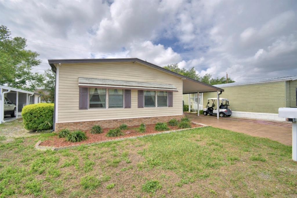 A single-story manufactured home with light siding, a brick base, and an attached carport — 4173 ROLLING OAKS DRIVE, WINTER HAVEN, FL