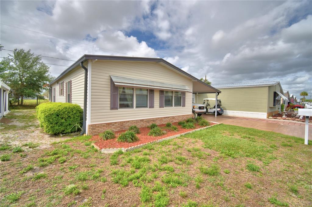 A beige mobile home with a brick base, metal awning, and a carport in front — 4173 ROLLING OAKS DRIVE, WINTER HAVEN, FL