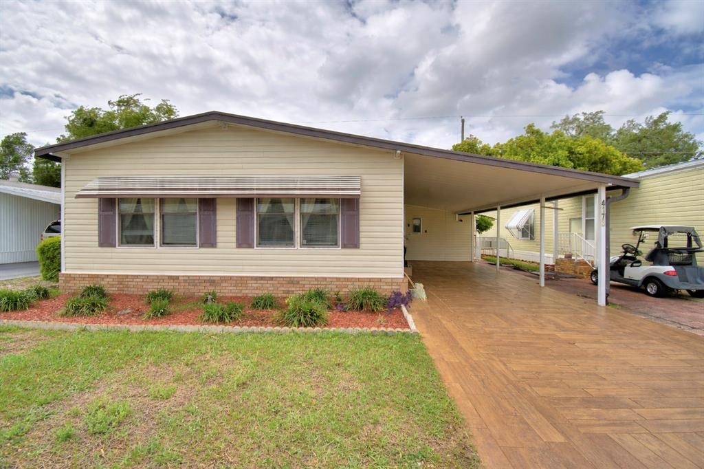 A single-story manufactured home with light siding, a brick base, and an attached carport — 4173 ROLLING OAKS DRIVE, WINTER HAVEN, FL