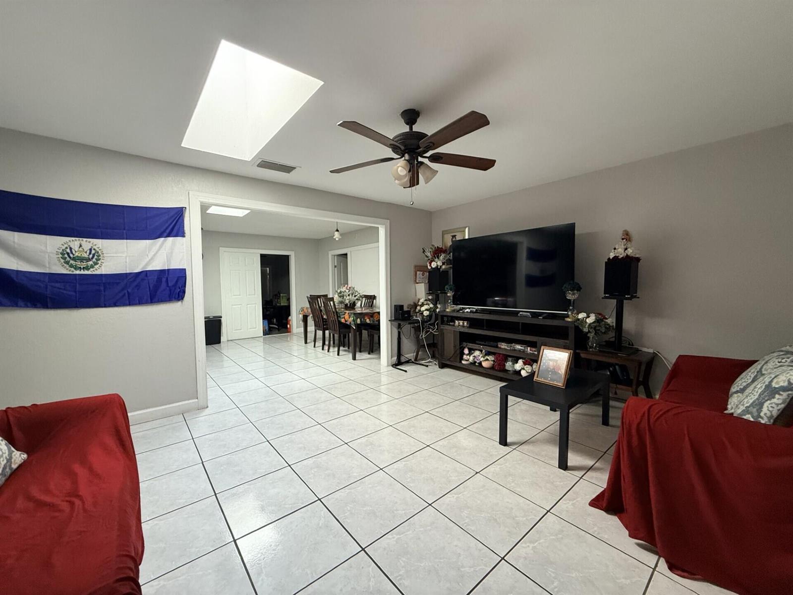 A living room with tile floors, a ceiling fan, a large television, and red furniture — 4904 Myrtle Drive, Fort Pierce FL 34982, FORT PIERCE, FL