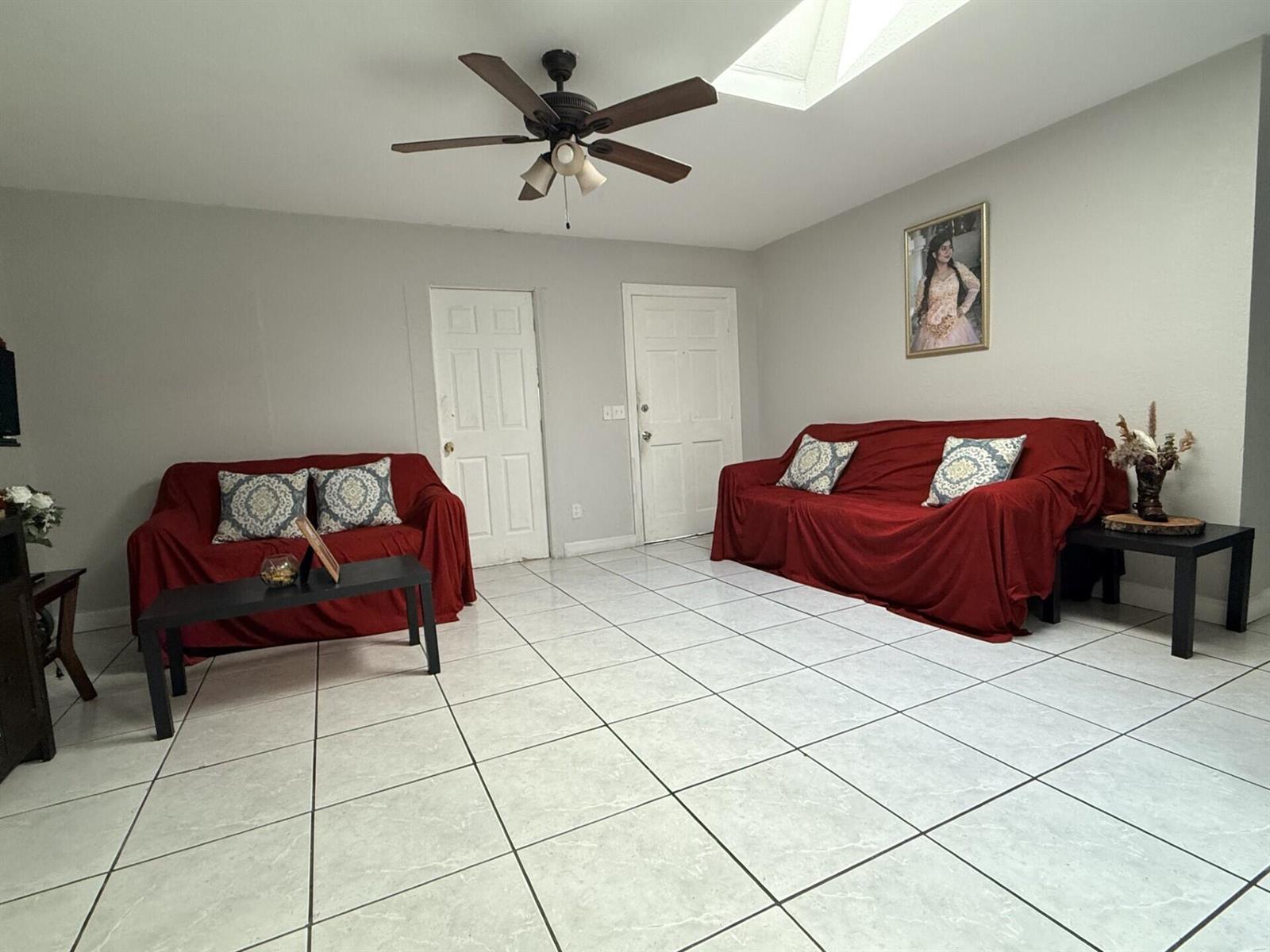 A living room features light gray walls, white tile flooring, two red sofas, and a ceiling fan — 4904 Myrtle Drive, Fort Pierce FL 34982, FORT PIERCE, FL