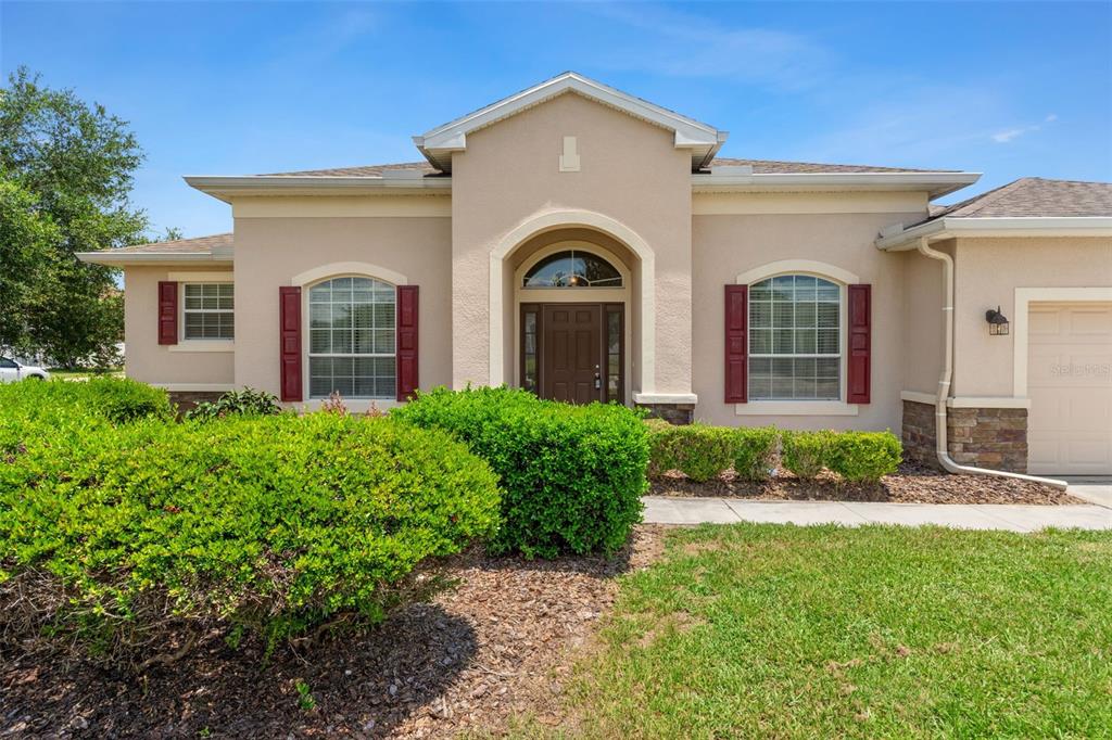 A single-story house with a beige stucco exterior, arched entryway, and red window shutters — 13589 HUNTERS POINT STREET, SPRING HILL, FL