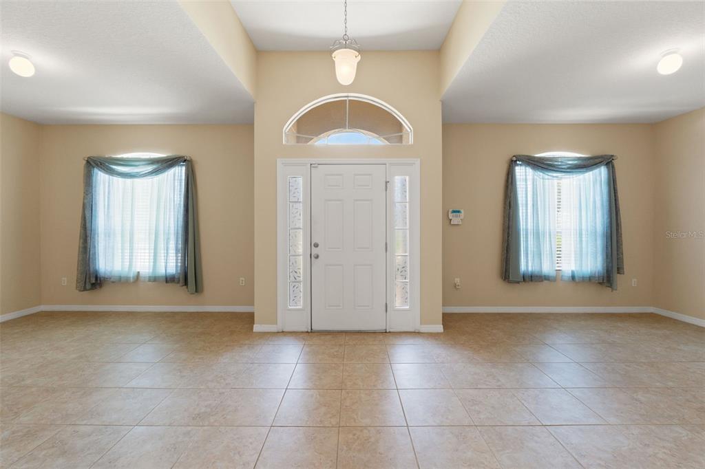 A bright foyer features beige tile floors, a white front door, and two side windows — 13589 HUNTERS POINT STREET, SPRING HILL, FL