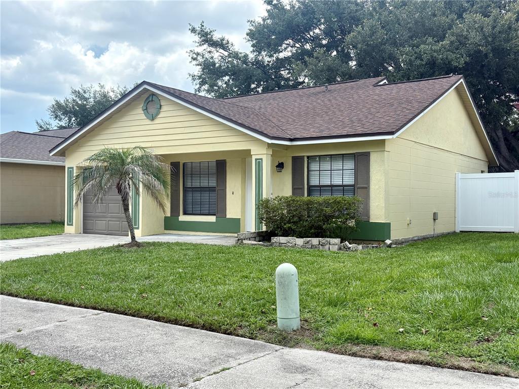 A single-story yellow house with a brown roof, a garage, and a small front lawn — 1021 ALPUG AVENUE, OVIEDO, FL