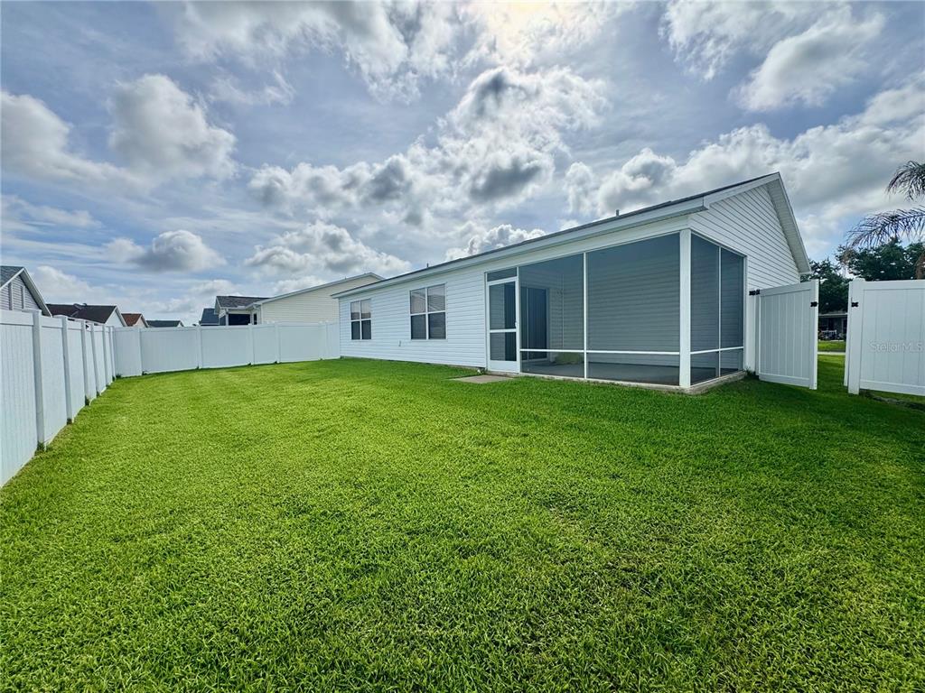 A backyard with a green lawn, white vinyl fencing, and a house with a screened-in porch — 892 NASH LOOP, THE VILLAGES, FL