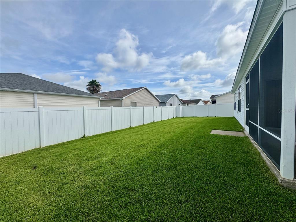 A fenced backyard features a green lawn and a screened-in patio area — 892 NASH LOOP, THE VILLAGES, FL