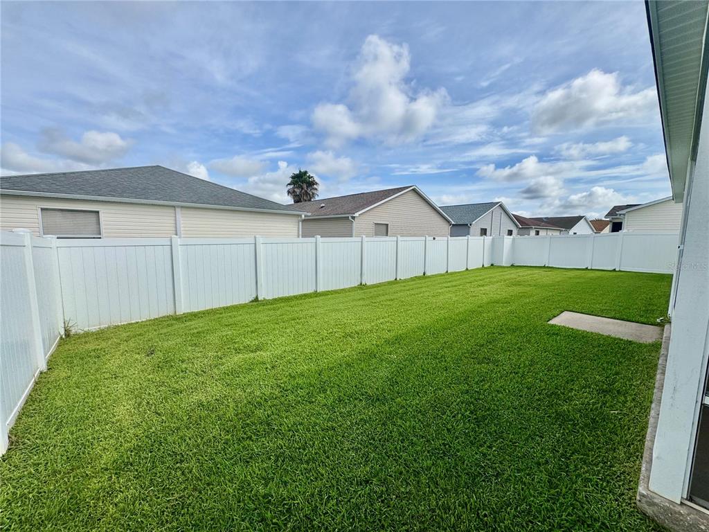 A fenced backyard with a green lawn and a concrete patio area — 892 NASH LOOP, THE VILLAGES, FL