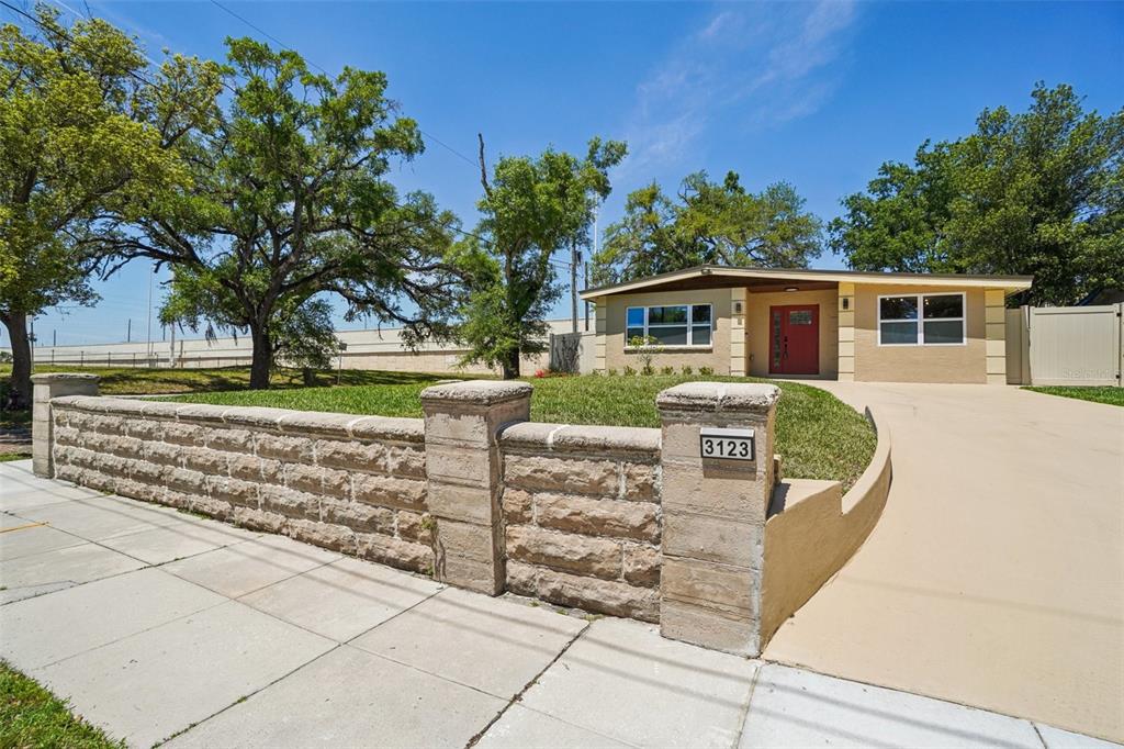 A single-story house with a red front door sits behind a stone retaining wall — 3123 W LA SALLE STREET, TAMPA, FL