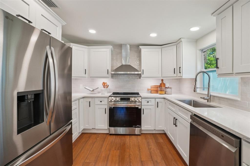 A modern kitchen features white cabinets, stainless steel appliances, light countertops, and wood-look flooring — 3123 W LA SALLE STREET, TAMPA, FL