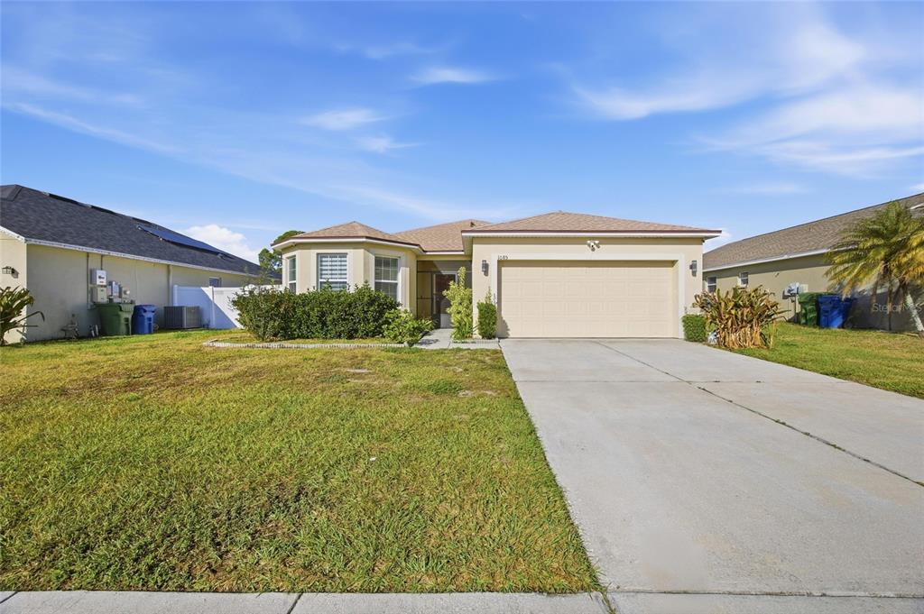 A single-story house with a beige stucco exterior, a two-car garage, and a front lawn — 1085 BRENTON MANOR DRIVE, WINTER HAVEN, FL
