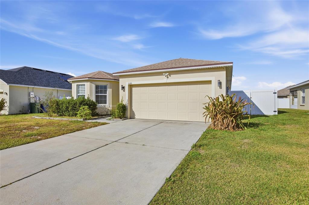 A single-story house with a beige stucco exterior, a two-car garage, and a concrete driveway — 1085 BRENTON MANOR DRIVE, WINTER HAVEN, FL