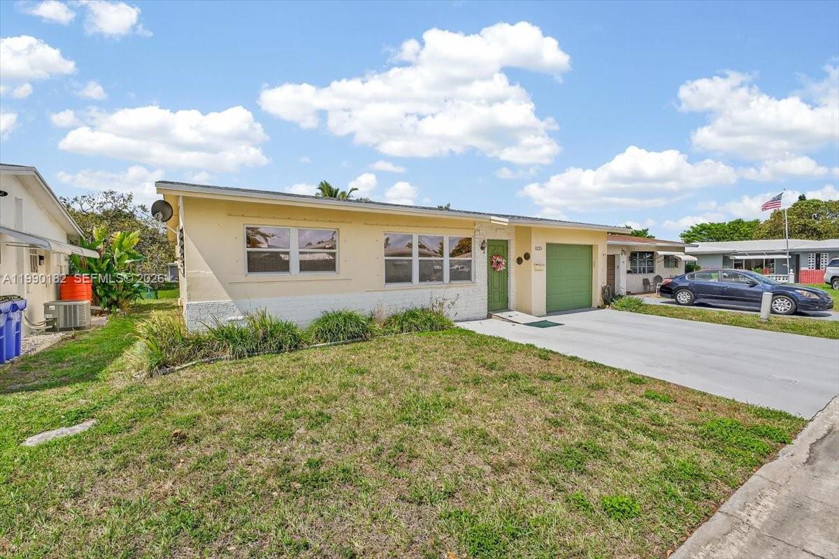 A single-story house with a light yellow exterior, green garage door, and a front lawn — 1125 NW 69th Ave, Margate FL 33063, MARGATE, FL