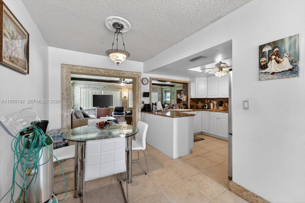 A dining area with a glass table sits adjacent to a kitchen with white cabinets — 1125 NW 69th Ave, Margate FL 33063, MARGATE, FL