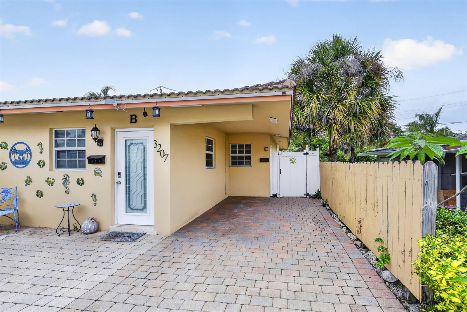 A yellow stucco exterior features a covered carport, a white front door, and a brick driveway — 3207 Marine Drive # A, Pompano Beach FL 33062, POMPANO BEACH, FL
