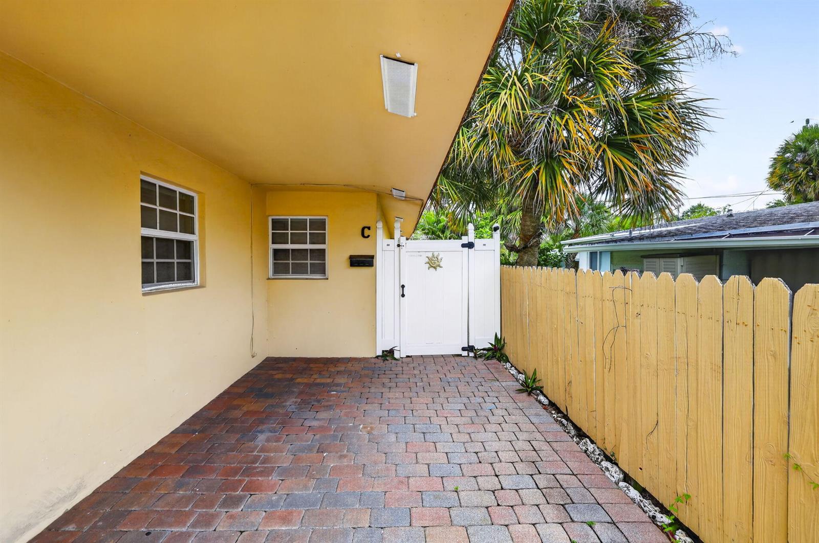 A paved patio area sits under a yellow overhang next to a white gate — 3207 Marine Drive # A, Pompano Beach FL 33062, POMPANO BEACH, FL