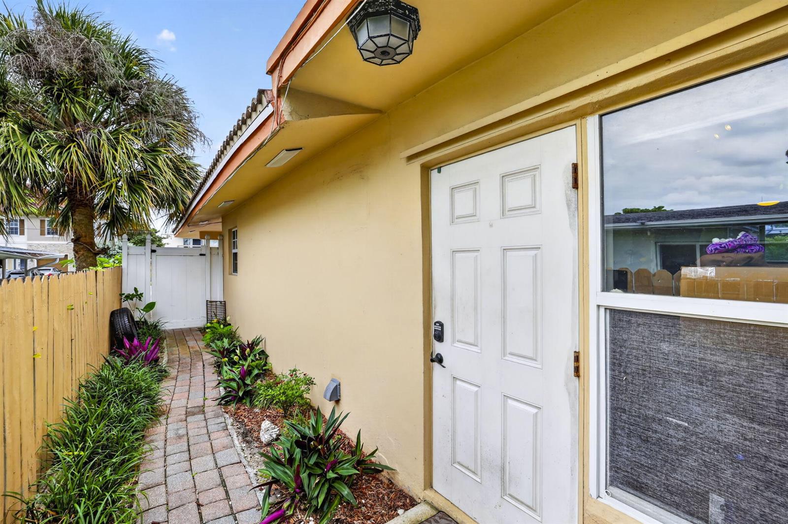 A brick walkway leads along the side of a house toward a white gate — 3207 Marine Drive # A, Pompano Beach FL 33062, POMPANO BEACH, FL