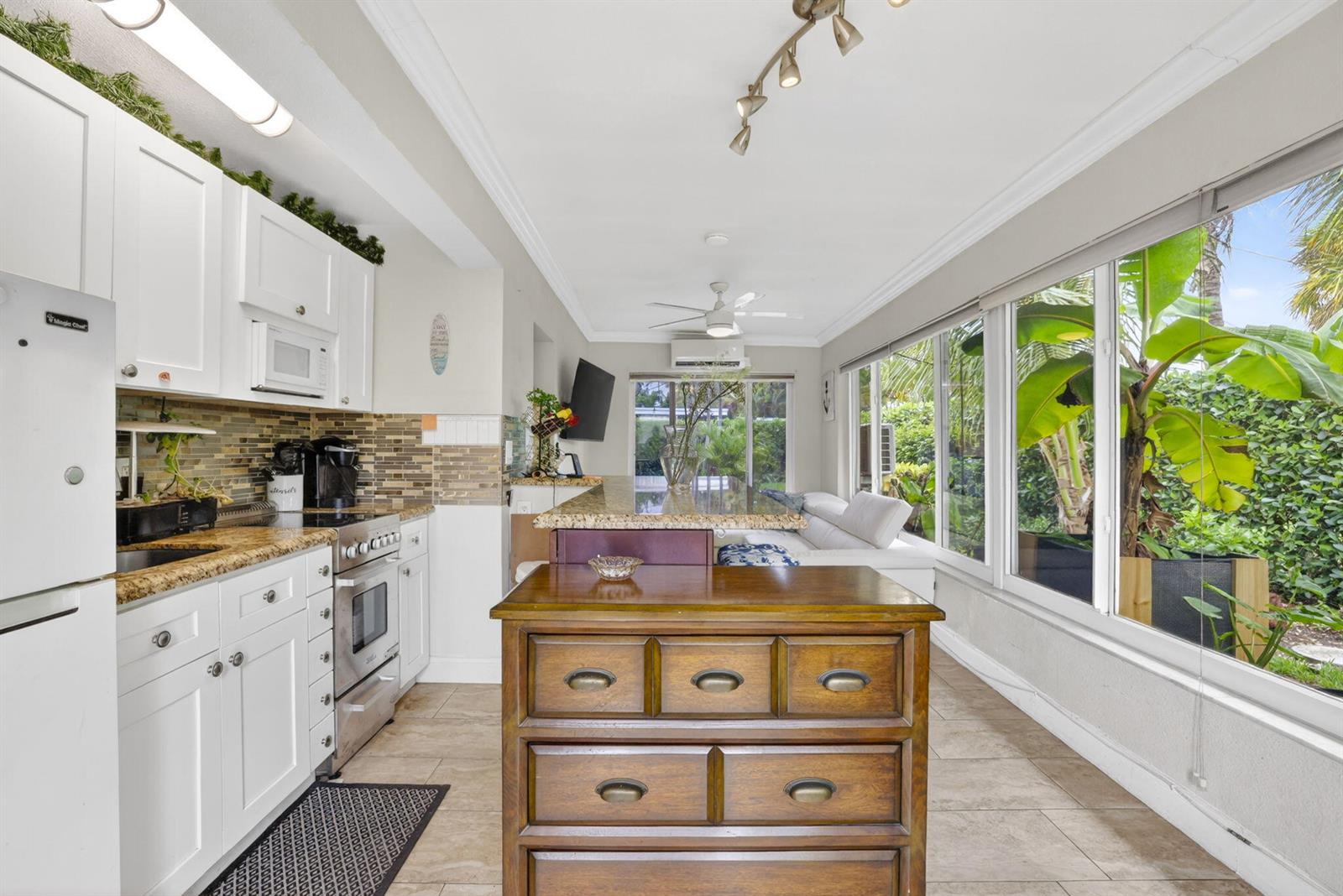 A kitchen features white cabinetry, a wooden island, granite countertops, and large windows overlooking greenery — 3207 Marine Drive # A, Pompano Beach FL 33062, POMPANO BEACH, FL