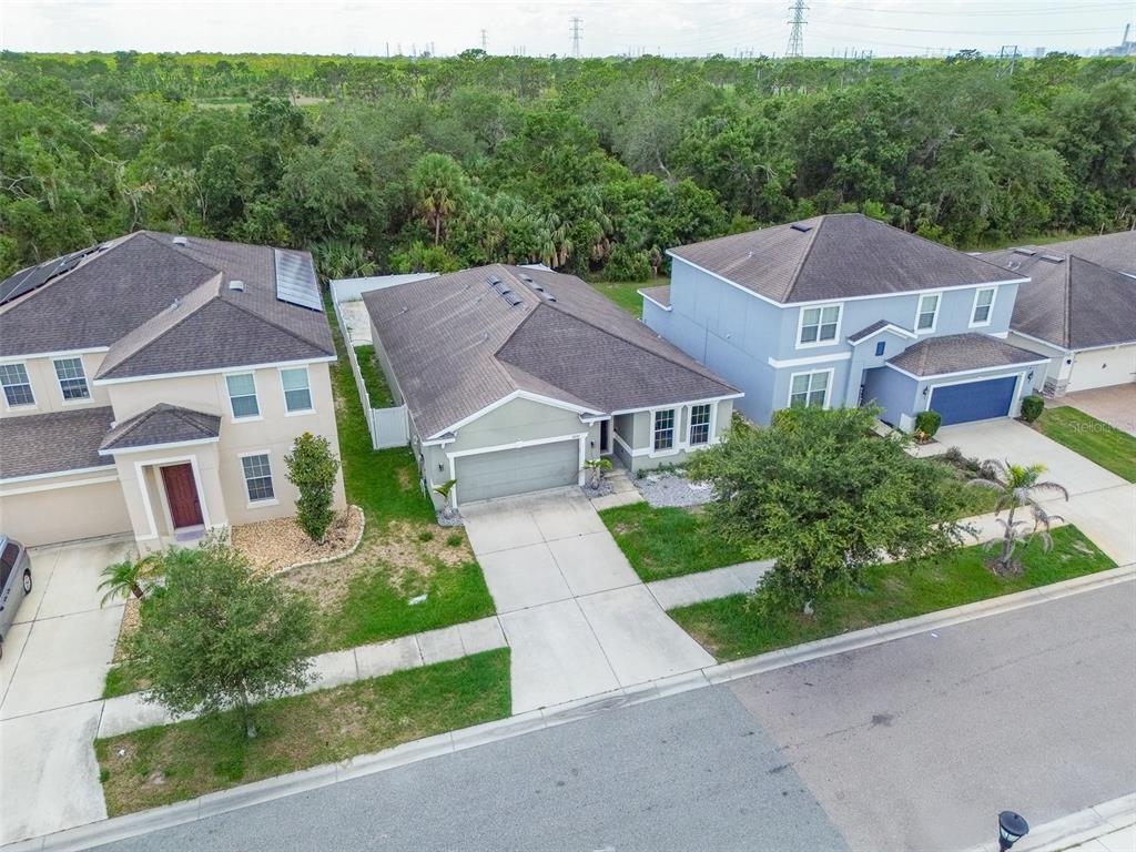 An aerial view shows three suburban houses with driveways and lawns bordering a wooded area — 12152 LEDBURY COMMONS DRIVE, GIBSONTON, FL