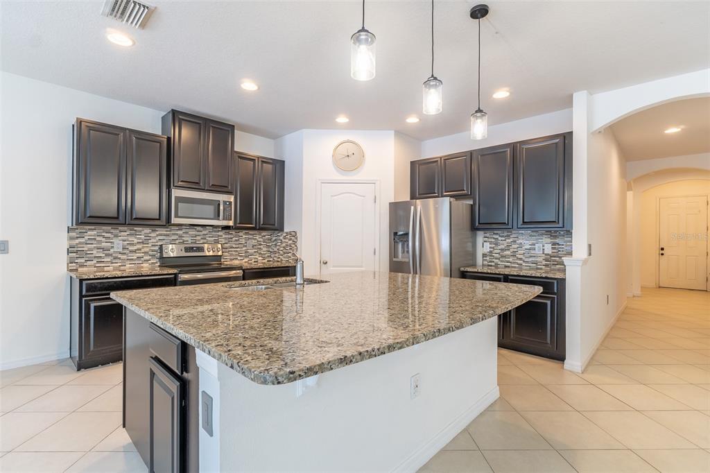 A kitchen features dark cabinetry, granite countertops, a central island, and a tiled backsplash — 12152 LEDBURY COMMONS DRIVE, GIBSONTON, FL