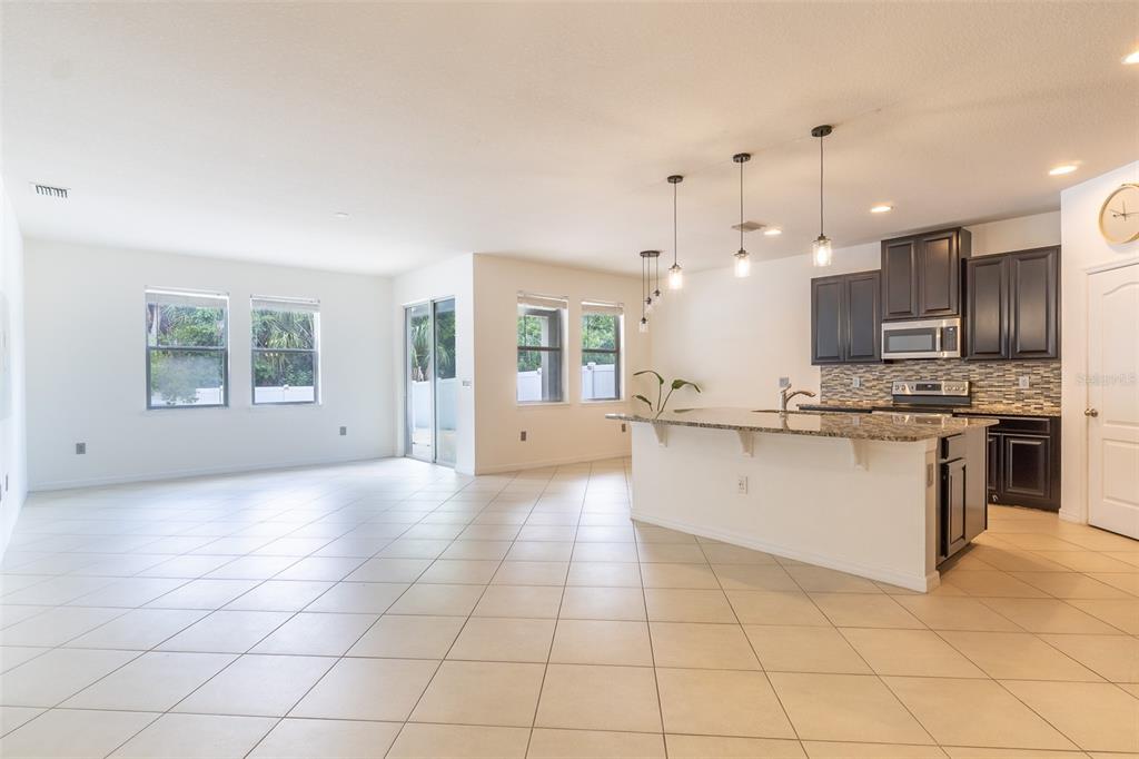 An open-concept kitchen and living area features tile flooring, dark cabinetry, and a granite island — 12152 LEDBURY COMMONS DRIVE, GIBSONTON, FL