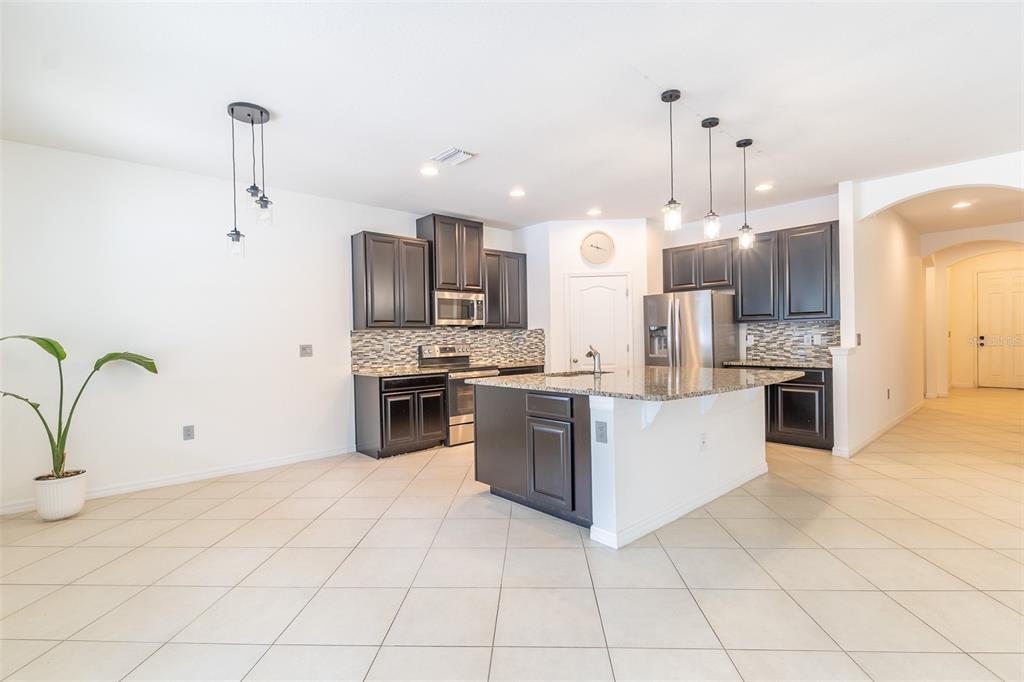 A kitchen features dark wood cabinets, granite countertops, a central island, and tile flooring — 12152 LEDBURY COMMONS DRIVE, GIBSONTON, FL
