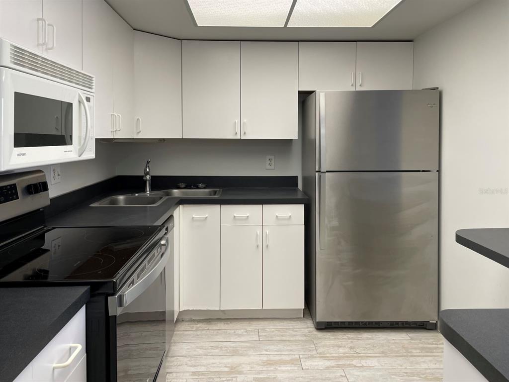 A kitchen features white cabinets, black countertops, stainless steel appliances, and light wood-look tile flooring — 4900 BRITTANY DRIVE S UNIT 509, ST PETERSBURG, FL