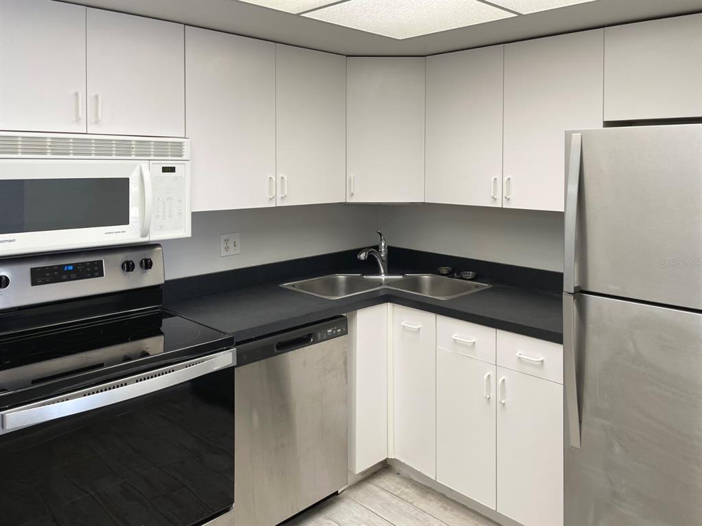 A kitchen features white cabinets, black countertops, stainless steel appliances, and a corner sink — 4900 BRITTANY DRIVE S UNIT 509, ST PETERSBURG, FL