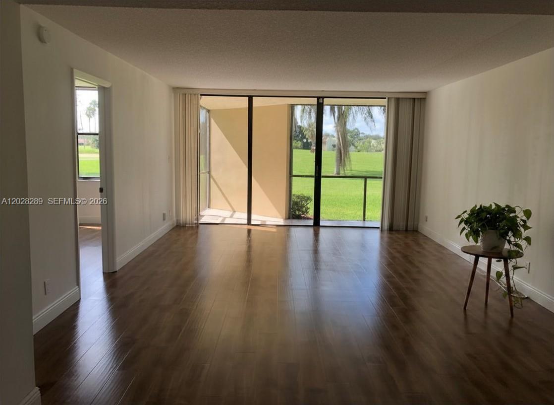 An empty living room features wood-look flooring, white walls, and a sliding glass door — 16300 Golf Club Rd # 105, Weston FL 33326, WESTON, FL