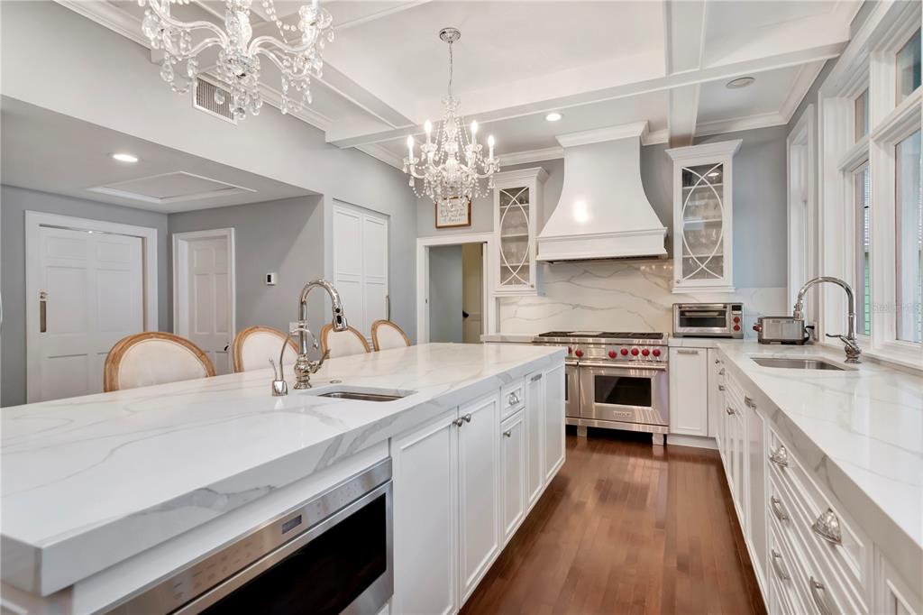 A bright kitchen features a large marble-topped island, white cabinetry, stainless steel appliances, and chandeliers — 6220 BAYSHORE BOULEVARD, TAMPA, FL