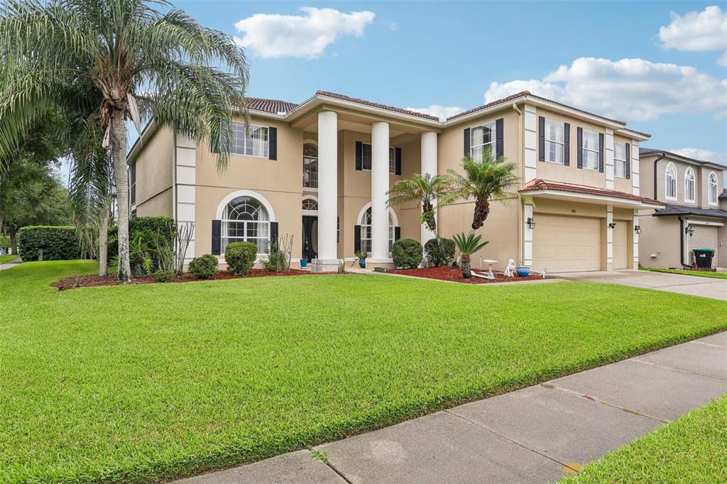 A two-story suburban house with a tan stucco exterior, white columns, and a three-car garage — 2626 TETON STONE RUN, ORLANDO, FL