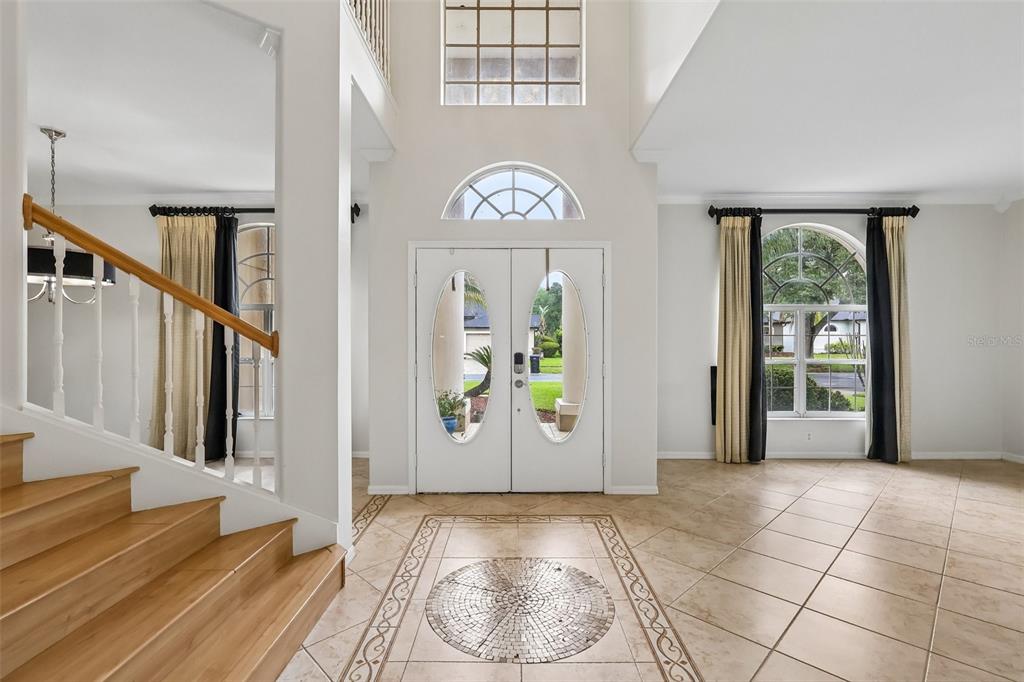 A bright two-story foyer features a tiled floor with a mosaic medallion and wooden stairs — 2626 TETON STONE RUN, ORLANDO, FL
