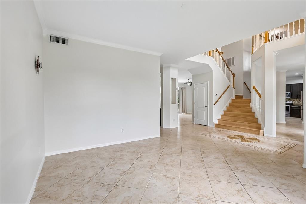 An open foyer features light tile flooring, a wooden staircase, and a view into the kitchen — 2626 TETON STONE RUN, ORLANDO, FL