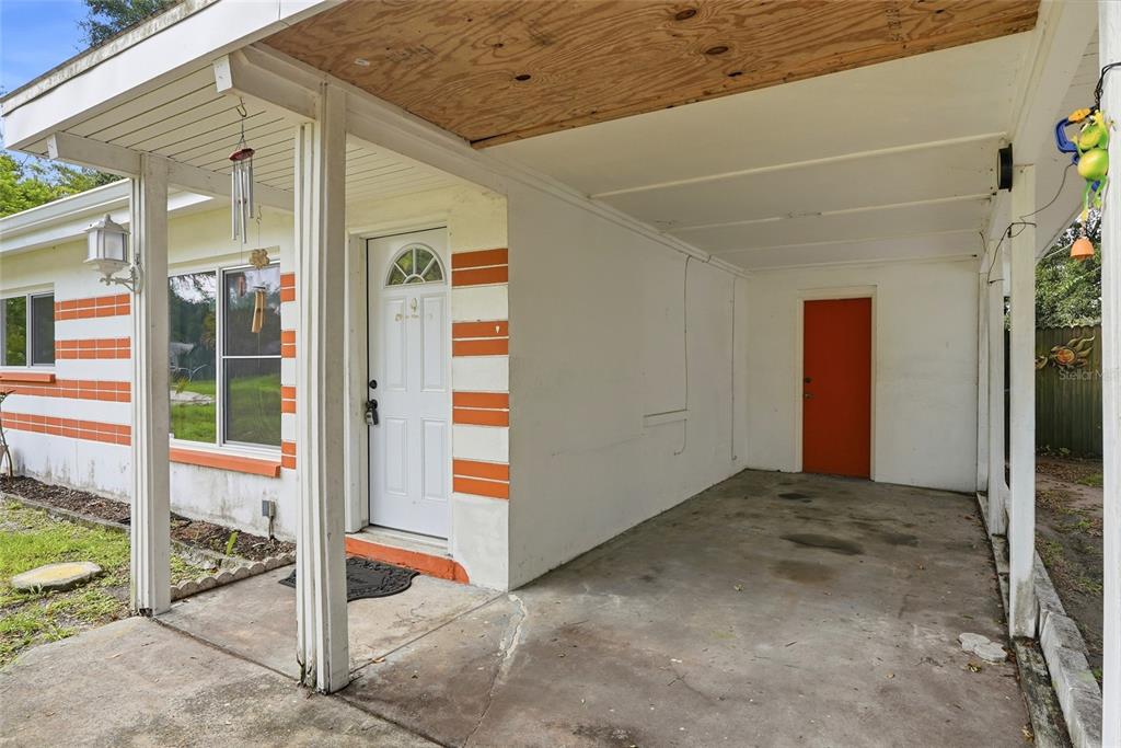 A white house exterior features a concrete carport, a white front door, and orange accents — 427 1ST AVENUE NE, LARGO, FL