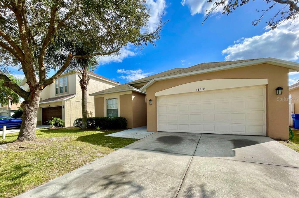 A tan, single-story suburban house with a two-car garage and a concrete driveway — 18417 MEADOW BLOSSOM LANE, TAMPA, FL