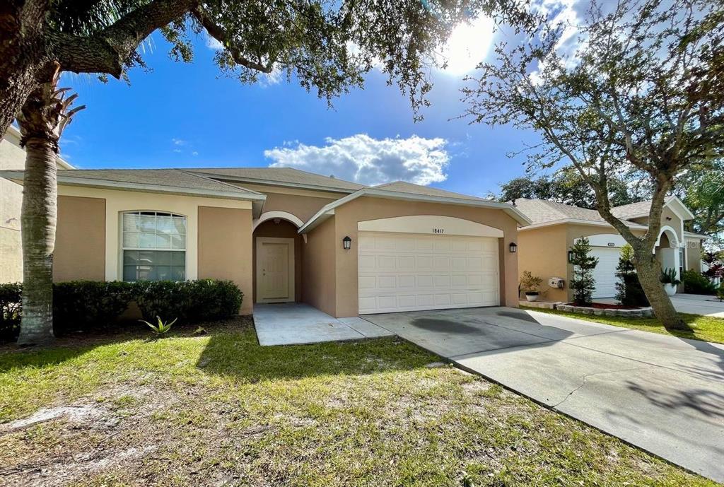 A single-story house with a beige stucco exterior, a two-car garage, and a concrete driveway — 18417 MEADOW BLOSSOM LANE, TAMPA, FL