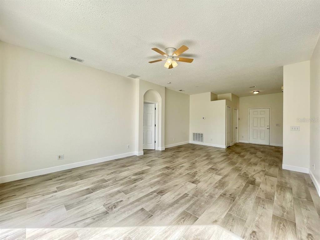 An empty living room features light-colored walls, a ceiling fan, and wood-look tile flooring — 18417 MEADOW BLOSSOM LANE, TAMPA, FL