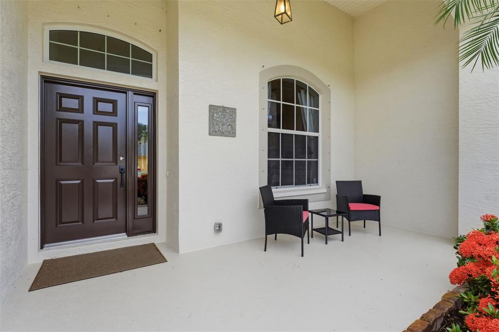 A covered front porch features a dark brown door, a window, and two wicker chairs — 12506 25TH COURT E, PARRISH, FL
