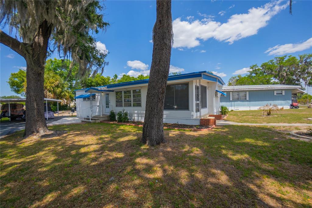 A white mobile home with a blue roof sits on a grassy lot with trees — 3896 PICCIOLA ROAD UNIT 554, FRUITLAND PARK, FL