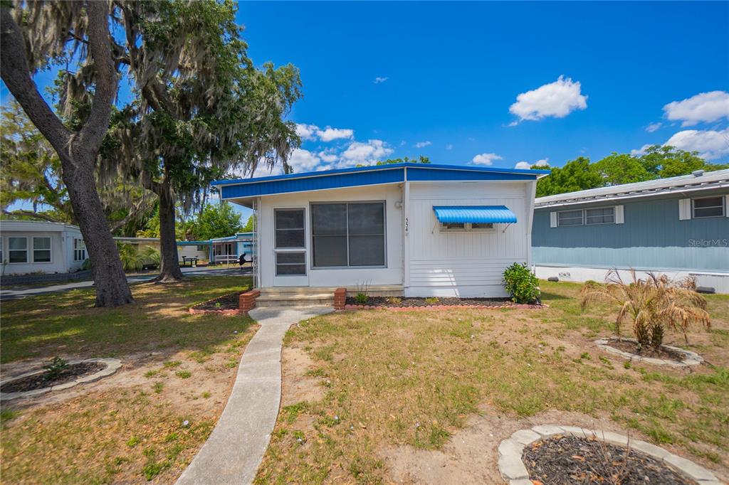 A white mobile home with a blue roof and trim sits on a grassy lot — 3896 PICCIOLA ROAD UNIT 554, FRUITLAND PARK, FL