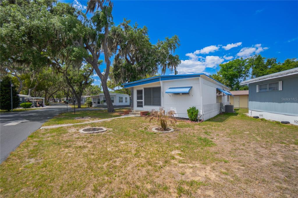 A white mobile home with blue trim sits on a grassy lot with large trees — 3896 PICCIOLA ROAD UNIT 554, FRUITLAND PARK, FL