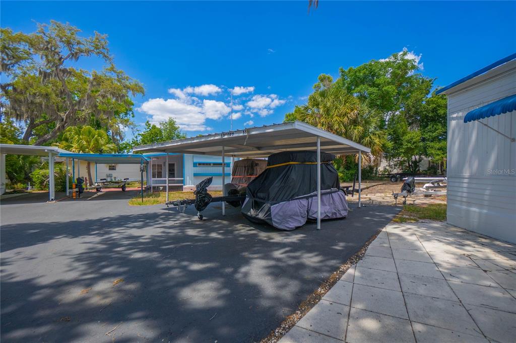 A paved driveway features a metal carport sheltering a covered golf cart and a trailer — 3896 PICCIOLA ROAD UNIT 554, FRUITLAND PARK, FL