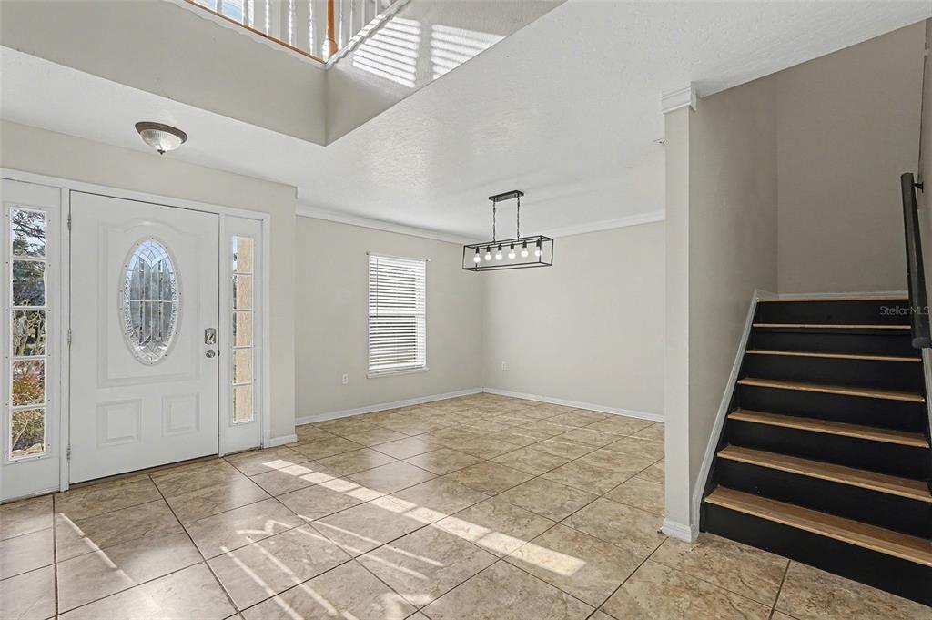 An entryway with tile flooring, a staircase, and a dining area with a modern chandelier — 194 ABALONE ROAD NW, PALM BAY, FL